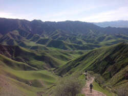 Photo of a person walking a path with green-colored mountains in the background